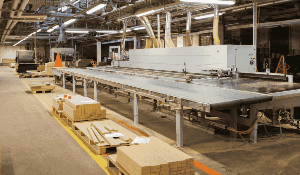 Park maszynowy w nowoczesnym zakładzie obróbki drewna. Widoczna linia produkcyjna do prefabrykacji mebli oraz przygotowane komponenty drewniane na paletach wzdłuż ciągu komunikacyjnego. Złudny spokój w branży meblarskiej: zmiany EUDR z grudnia 2025 r.
