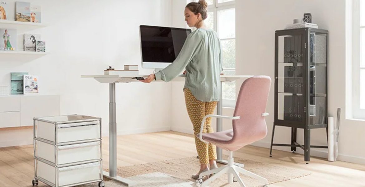 Projekt domowego biura: kobieta pracująca przy biurku z regulowaną wysokością biurka, różowe krzesło.