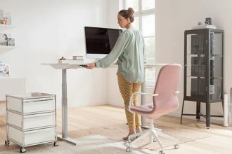 Projekt domowego biura: kobieta pracująca przy biurku z regulowaną wysokością biurka, różowe krzesło.