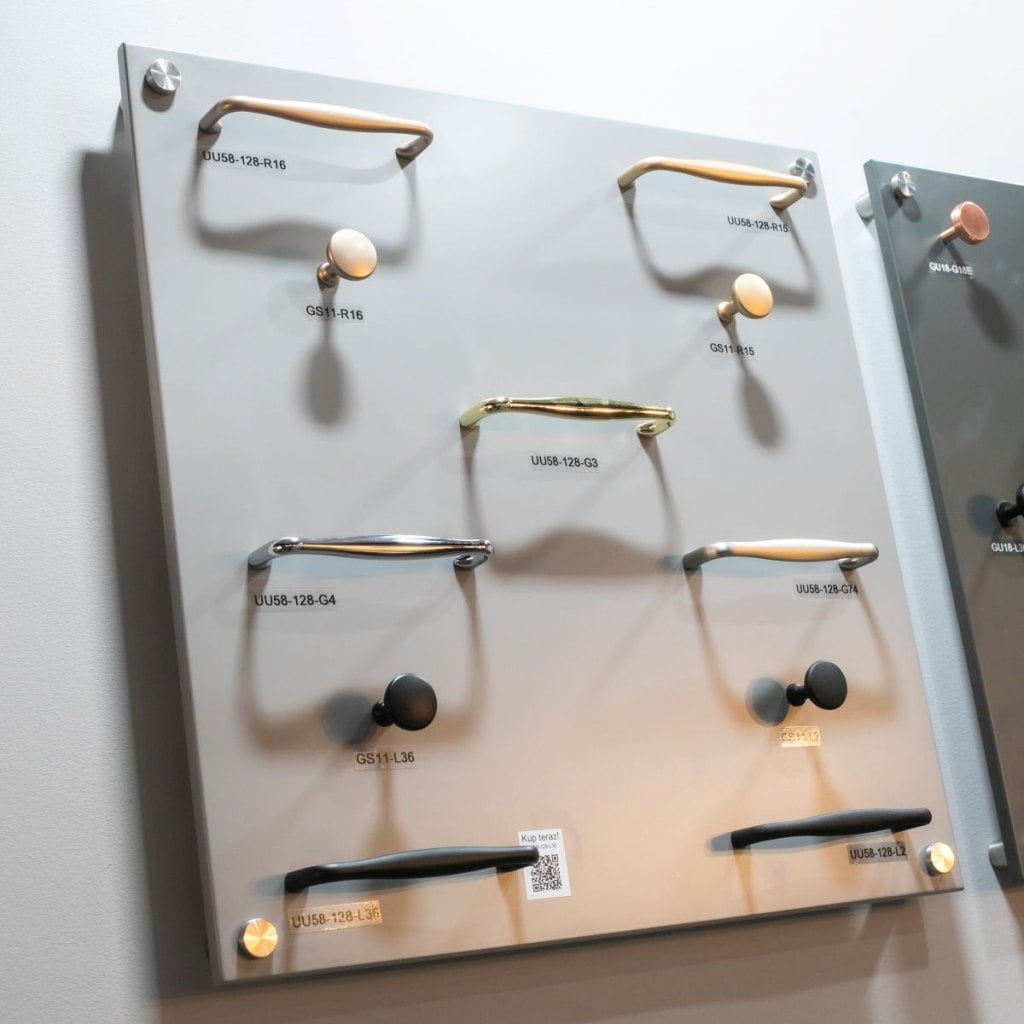 Złote i czarne uchwyty oraz gałki meblowe firmy Gamet prezentowane na szarej ściance podczas tragów  Warsaw Home & Contract 2021 - miesięcznik i portal informacyjny branży meblarskiej biznes.meble.pl