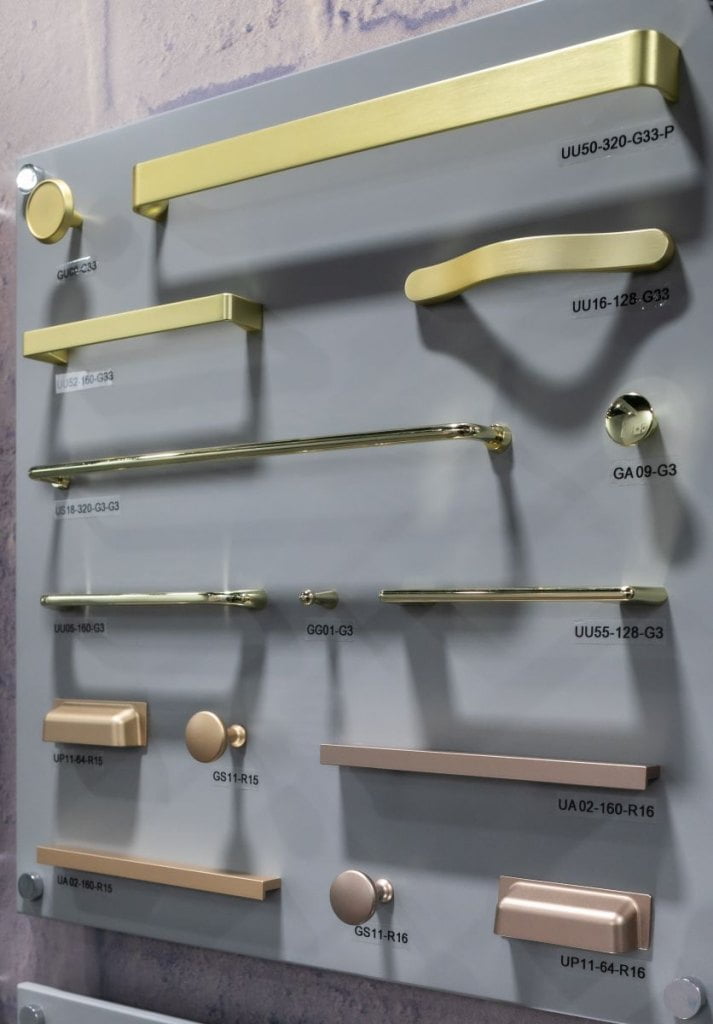 Uchwyty i gałki firmy Gamet w odcieniach złota prezentowane na szarej ściance podczas tragów  Warsaw Home & Contract 2021 - miesięcznik i portal informacyjny branży meblarskiej biznes.meble.pl