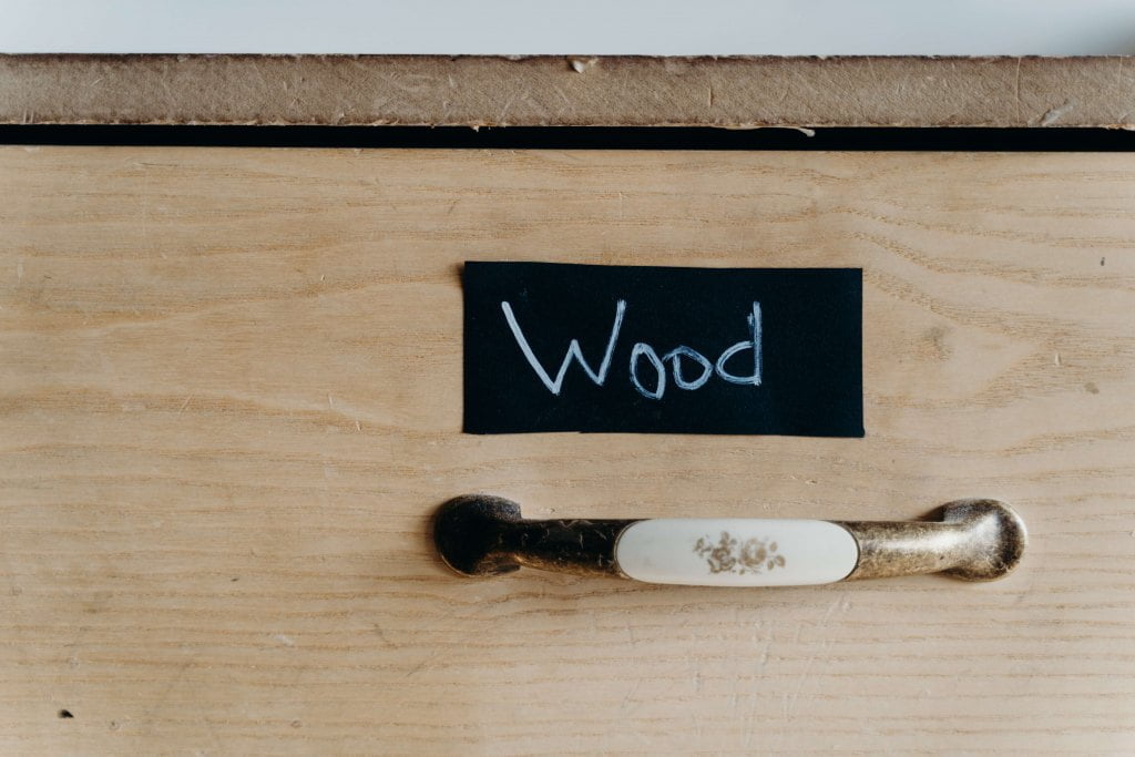 Biały metalowy uchwyt porcelanowy ze wzorkiem kwiatowym na drewnianej szafce z napisem „Wood”.