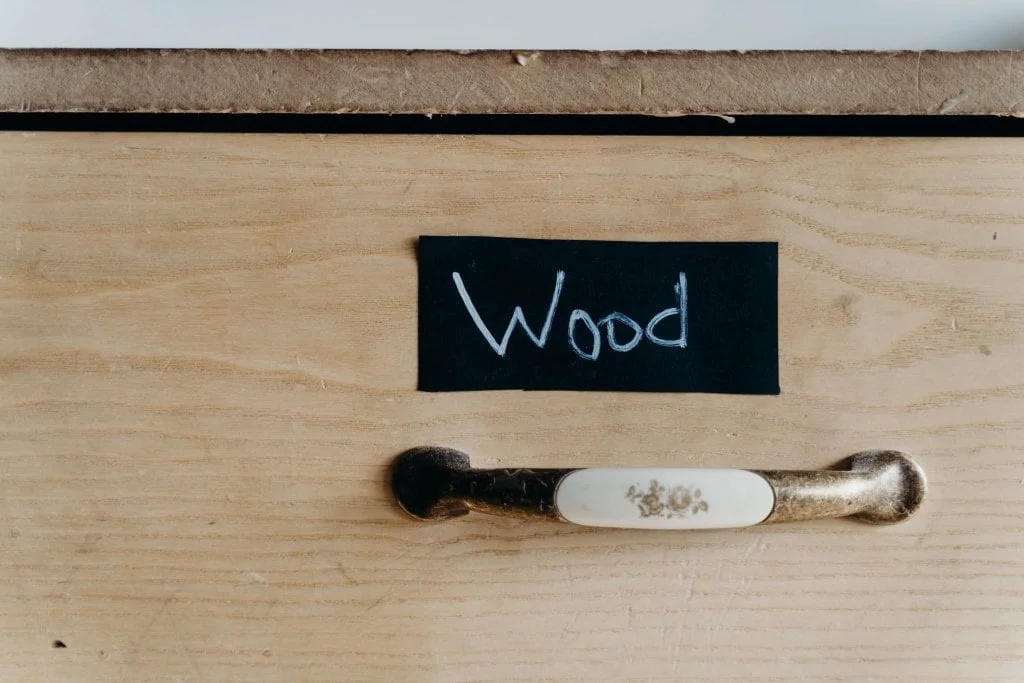 Biały metalowy uchwyt porcelanowy ze wzorkiem kwiatowym na drewnianej szafce z napisem „Wood”.