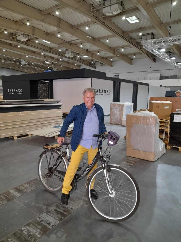 Rower ułatwia Józefowi Szyszce doglądanie montażu targów w dziewięciu pawilonach. Kolory ubrania są nieprzypadkowe – zdjęcie pochodzi z przygotowań do edycji targów w maju 2022, krótko po wybuchu wojny w Ukrainie, której przedstawiciele w tamtym roku po raz pierwszy zorganizowali zbiorowe stoisko narodowe na targach MEBLE POLSKA.