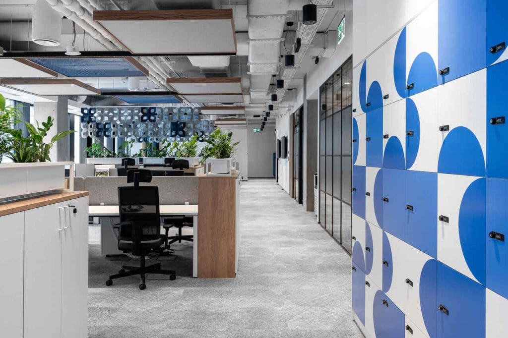 Część pracownicza biura Hoogwegt w Warszawie spod kreski BIT CREATIVE, na którą składa sią open space oraz pomieszczenia biurowe, to przede wszystkim jasne wnętrza, ocieplone drewnem, z kolorystycznymi akcentami w formie lakierowanej siatki cięto-ciągnionej na suficie czy kolorowych frontów lockerów. Przestrzenie te zróżnicowano poprzez dobranie innych wzorów tapet do gabinetów i do open space’ów. Całość wystroju uzupełnia duża ilość żywej zieleni w wolnostojących oraz stojących na szafkach donicach. Fot. Fotomohito.