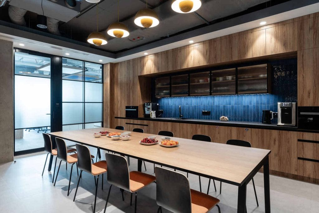 Na uwagę zasługuje także pomieszczenie socjalne z aneksem kuchennym. Jego kolorystyka oraz materiały wykończeniowe pomieszczenia również nawiązują do klimatu całości aranżacji. W kuchni utrzymaliśmy prostą posadzkę oraz otwarty sufit, gdzie jedynie strop pomalowany jest na biało. W zabudowie kuchennej uwagę przyciągają granatowe płytki o różnorodnym wybarwieniu i fronty ze szkła ryflowanego. Z kolei na dwóch przeciwległych ścianach charakterystycznym punktem są dekoracyjne kinkiety umieszczone w osiach okładziny drewnopodobnej. W ten sposób miejsce to staje się mniej formalnym, a jednak ciągle utrzymanym w tej samej tonacji stylistycznej, punktem spotkań pracowników – podsumowuje realizację dla firmy Hoogwegt arch. Jakub Bubel z pracowni BIT CREATIVE. Fot. Fotomohito.