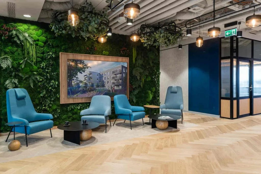 Projekt biura zrealizowany przez BIT CREATIVE został dopasowany do identyfikacji wizualnej Bouygues Immobilier Polska, co znalazło odzwierciedlenie w wykorzystanych kolorach, materiałach oraz elementach dekoracyjnych. Flagowe kolory marki, takie jak odcienie niebieskiego i szarości, zostały harmonijnie wplecione w wystrój wnętrz, nadając przestrzeni elegancji, a jednocześnie podkreślając jej przyjazny charakter. Subtelne nawiązania do logo i filozofii firmy pojawiają się w detalach, takich jak grafiki na ścianach czy wykończenia mebli, wzmacniając wizerunek marki. Fot. Fotomohito.