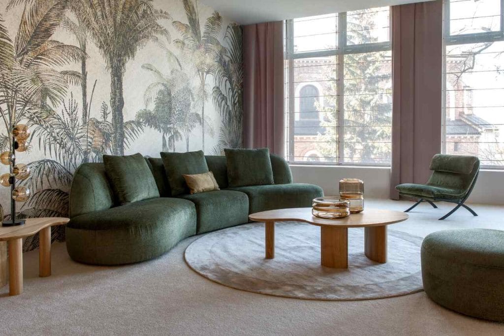 Narożnik Sirena marki KLER, której salon znajduje się na terenie Galerii Wnętrz DOMAR, przyciąga uwagę ponadczasową formą oraz tkaniną z kolekcji Accadia w szlachetnym, zielonym odcieniu. Dzięki modułowej konstrukcji z trzech brył (bez klasycznych podłokietników) zapewnia więcej miejsca do siedzenia i daje możliwość tworzenia różnych układów. Wysokiej jakości pianki, włókniny i sprężyny w siedziskach oraz oparciach gwarantują komfort i trwałość. Narożnik ma 345 cm szerokości, 146 cm głębokości i 93 cm wysokości, przez co doskonale sprawdzi się w przestronnym salonie lub eleganckim gabinecie. W zestawie dostępny jest również dopasowany puf.