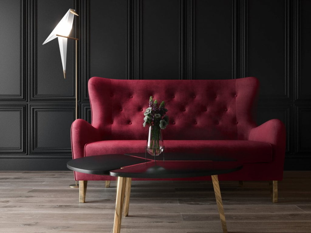 Sofa w karminowej czerwieni na tle ściany ze sztukaterią.