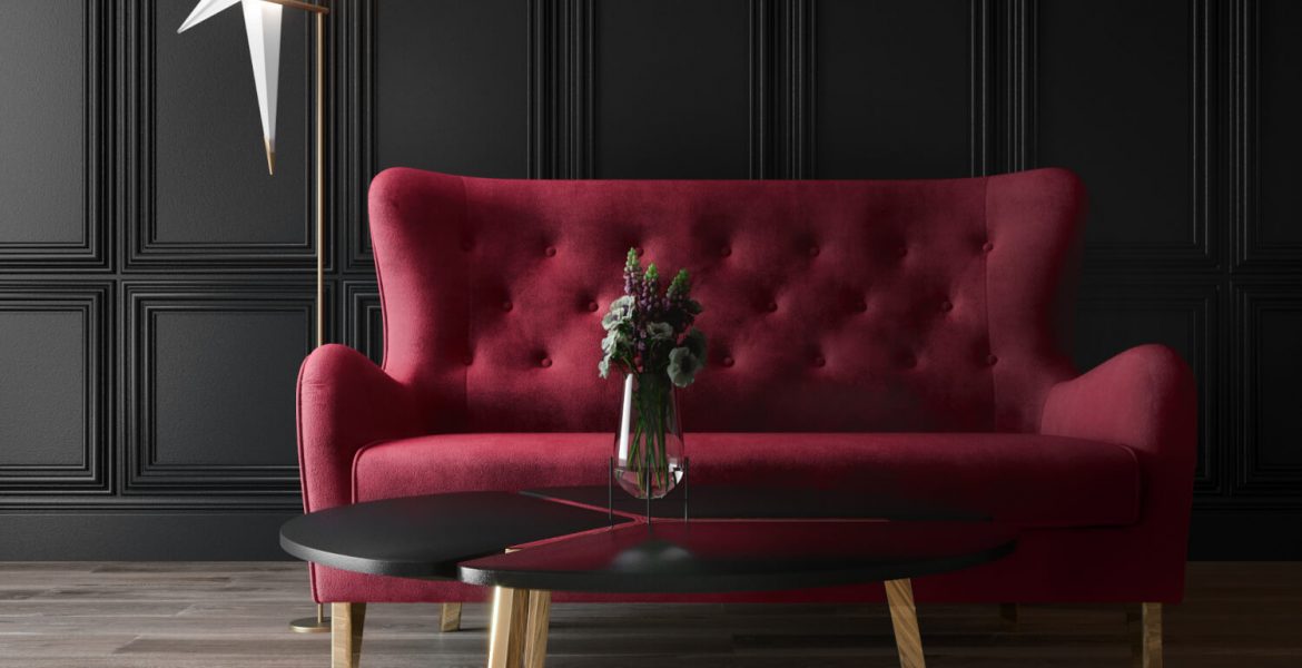 Sofa w karminowej czerwieni na tle ściany ze sztukaterią.