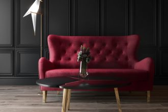 Sofa w karminowej czerwieni na tle ściany ze sztukaterią.