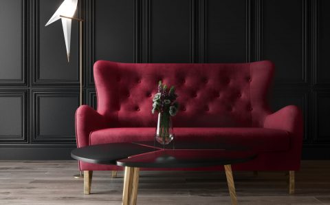 Sofa w karminowej czerwieni na tle ściany ze sztukaterią.