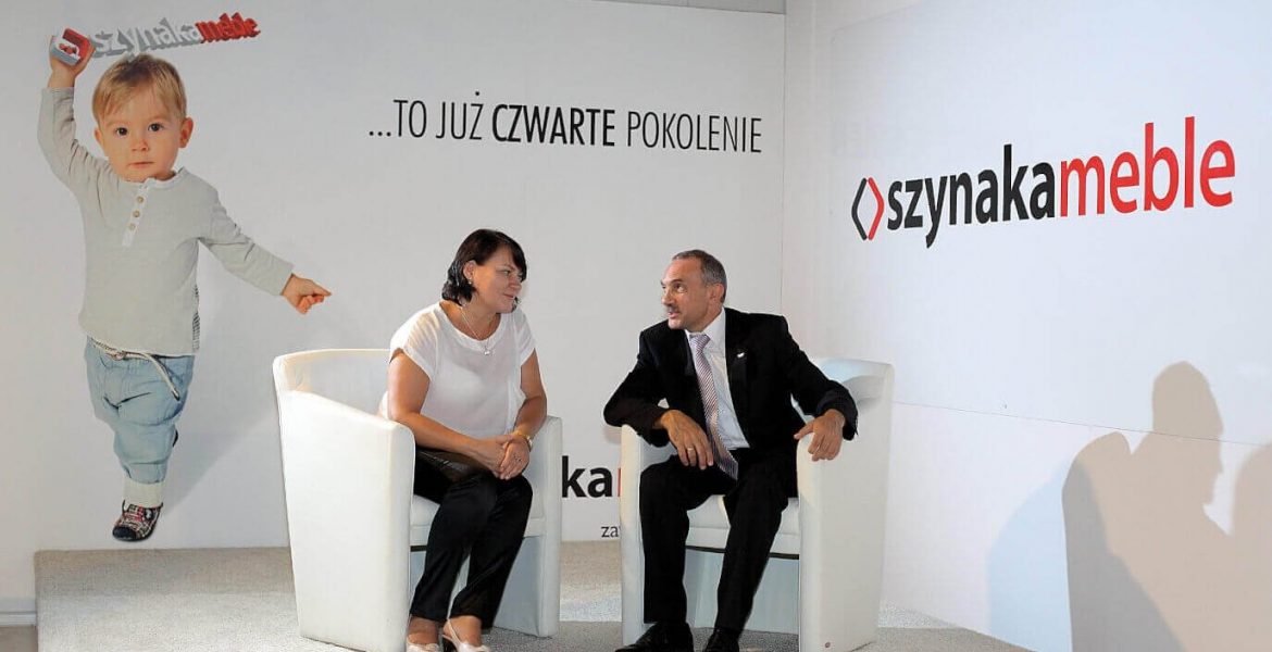 Alina i Jan Szynaka podczas Targów Partnerskich Szynaka Meble, w tle wnuk Antoś, Iława, 2013 r.