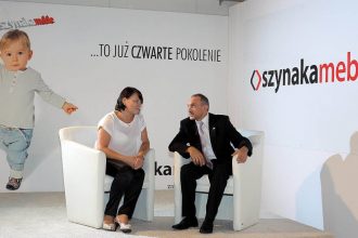 Alina i Jan Szynaka podczas Targów Partnerskich Szynaka Meble, w tle wnuk Antoś, Iława, 2013 r.