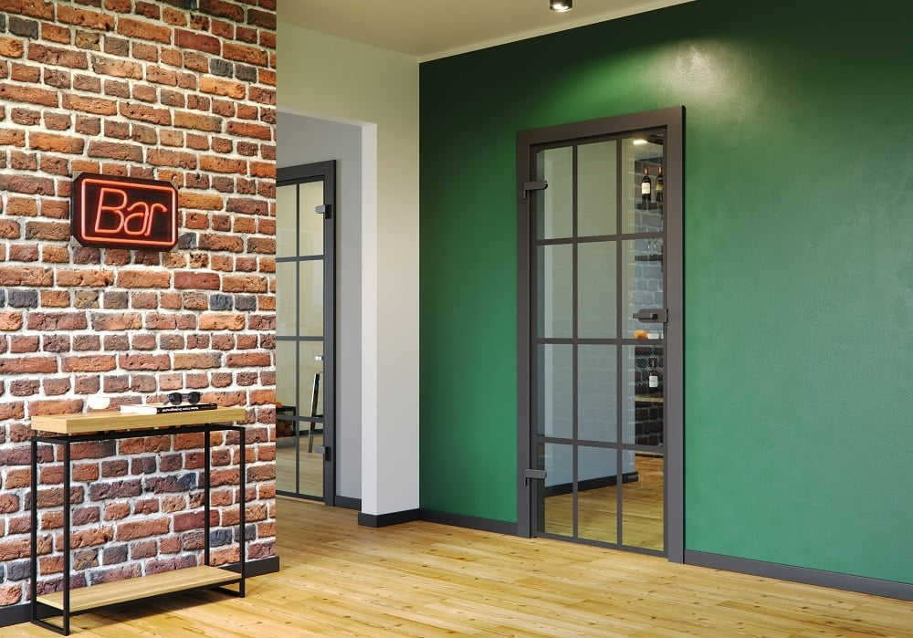 Porta drzwi - loftowe drzwi wewnętrzne Glass tafla przezroczysta Supermatt czarny z czarnymi okuciami na zielonej ścianie - miesięcznik i portal informacyjny branży meblarskiej biznes.meble.pl