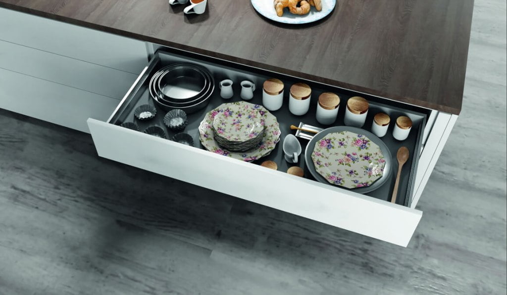 Otwarta szuflada z talerzami i pojemnikami na prowadnicach F70 firmy Salice w białej kuchni z brązowym blatem - miesięcznik i portal informacyjny branży meblarskiej biznes.meble.pl