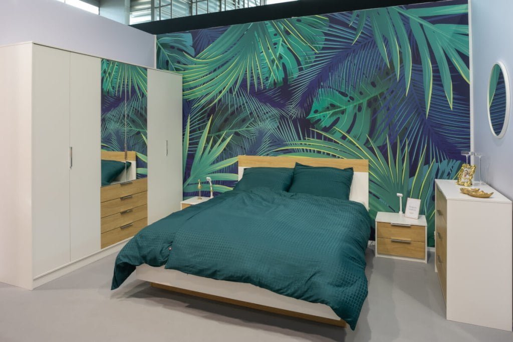 Sypialnia Galaxy w kolorze biały i jasnego drewna (łóżko z zieloną pościelą, szafa z lustrem i szufladami, dwie szafki nocne) zaprezentowana na stoisku firmy Idźczak Meble na targach Meble Polska 2023 w Poznaniu - miesięcznik i portal informacyjny branży meblarskiej biznes.meble.pl