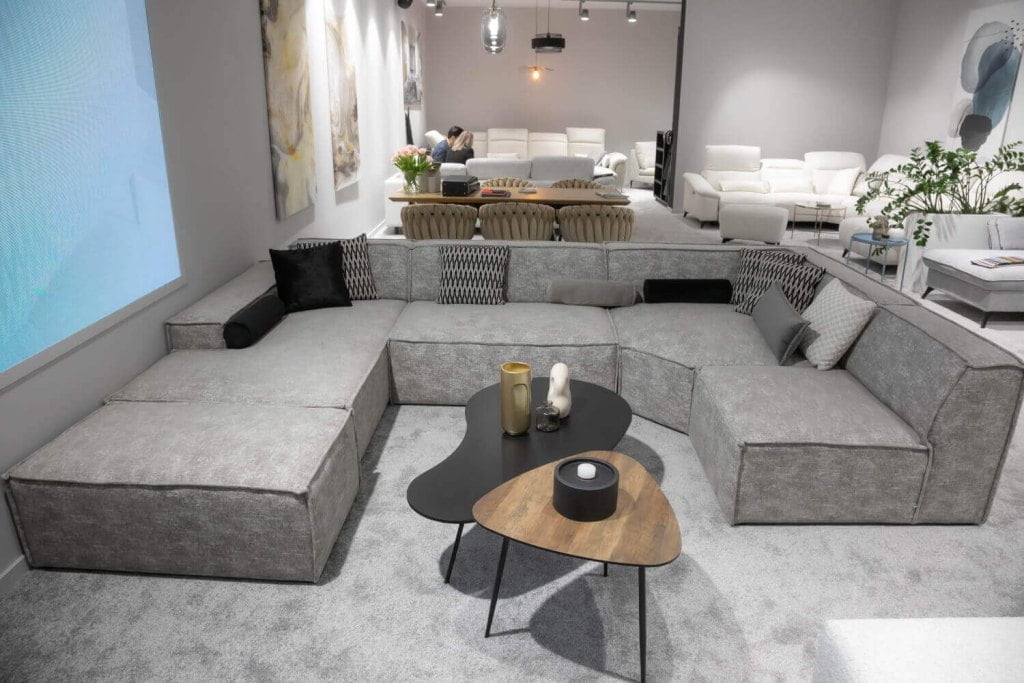 Narożnik Fondy w kolorze szarym z czarnymi i szarymi poduszkami firmy Stagra Meble zaprezentowany podczas targów Meble Polska 2023 w Poznaniu - miesięcznik i portal informacyjny branży meblarskiej biznes.meble.pl