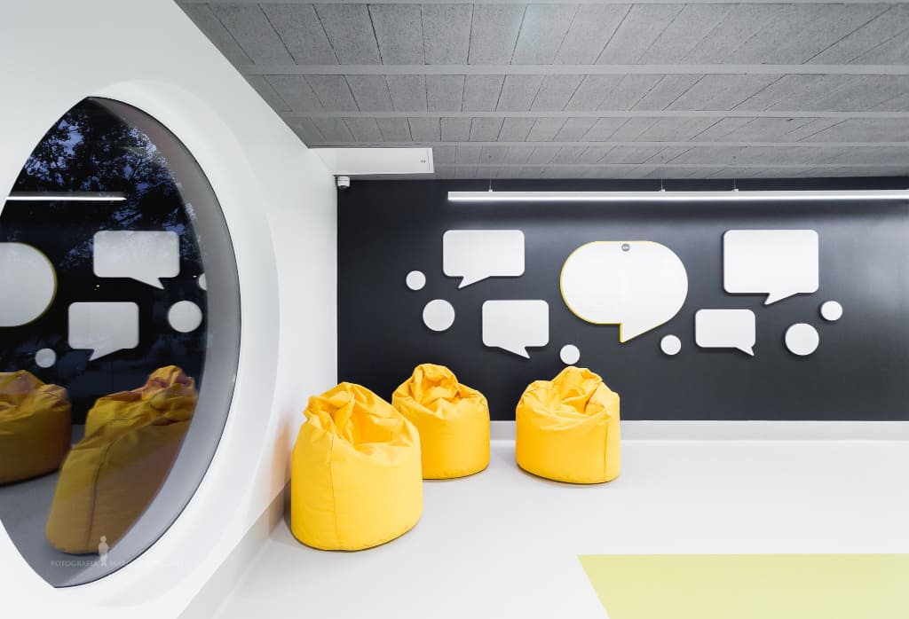 Strefa relaksu w holu na piętrze z tablicami pomysłów i informacji oraz wygodnymi pufami.