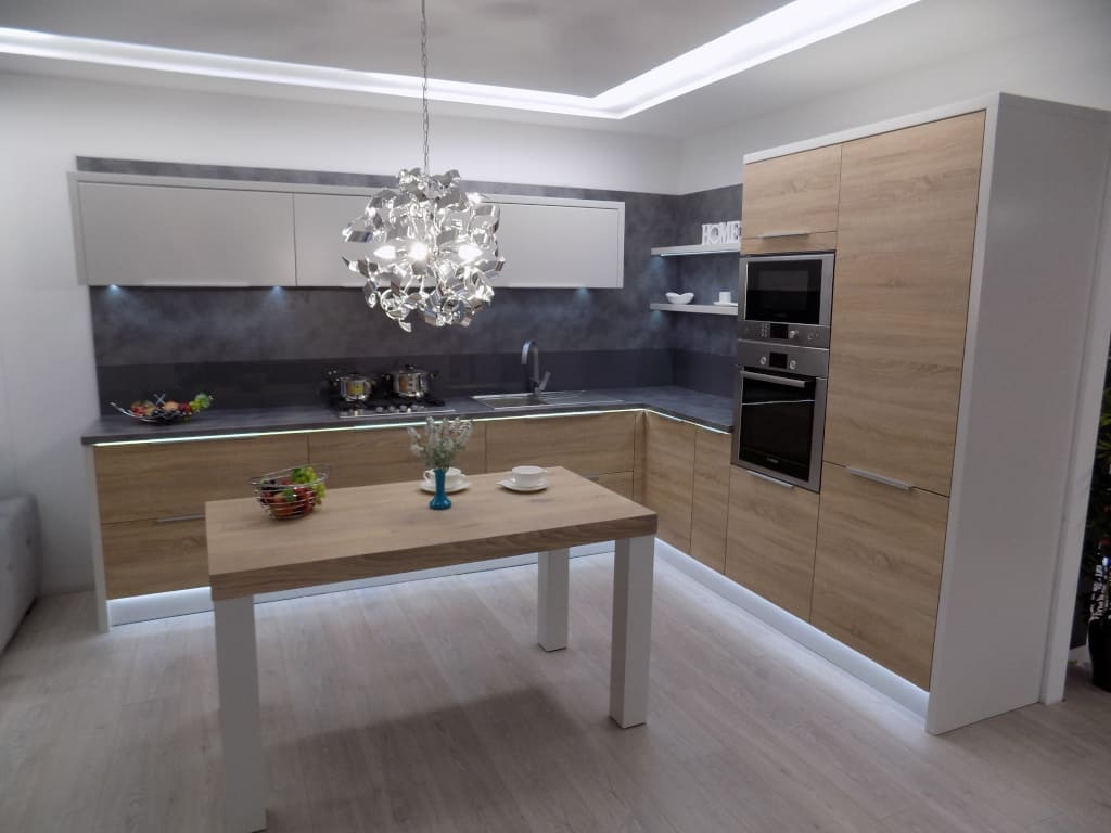 Płyty ścienne w kolorze betonu, jasne drewnopodobne fronty i biała zabudowa szafek górnych – to wszystko tworzy tę przytulną kuchnię firmy Mebles Design.