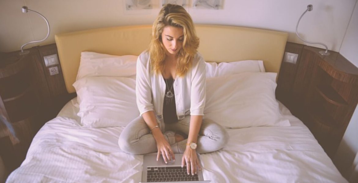 Kobieta z laptopem na łóżku w sypialni.
