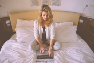 Kobieta z laptopem na łóżku w sypialni.