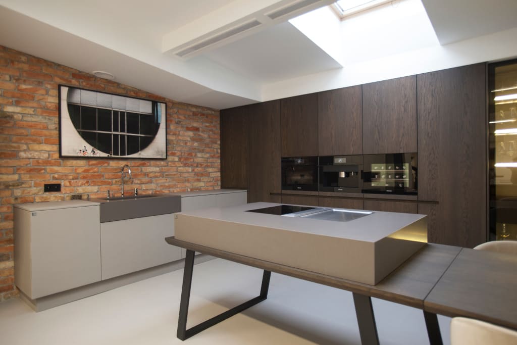 Szare meble kuchenne pokryte multifunkcjonalną zaprawą kwarcową „Ecomalta” to jedna z realizacji Studia Prostych Form. Na stole: płyta ze zintegrowanym w blacie pochłaniaczem firmy Bora.