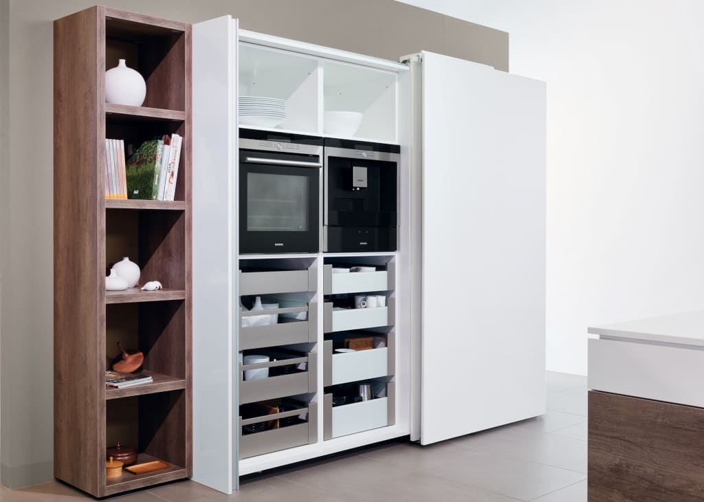 Urządzenia AGD oraz regały z zapasami sprytnie chowają się za drzwiami przesuwnymi, pozostawiając na widoku elegancką i uprzątniętą kuchnię.