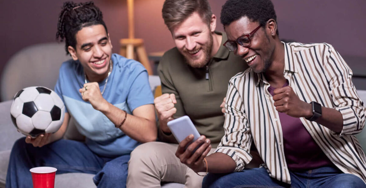 Orion Media - bukmacher, zakłady, zawód Typer - trzech mężczyzn siedzących na kanapie oglądających mecz na żywo przez smartfon