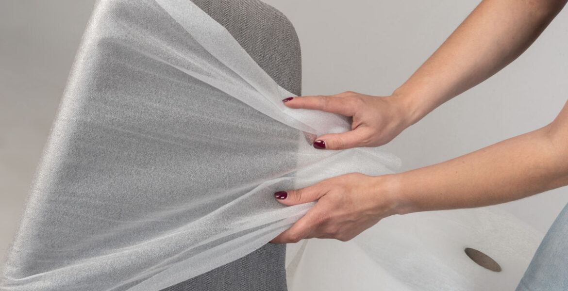 Szare krzesło biurowe, które owijane jest przez kobietę folią polietylenową.