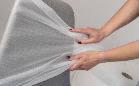 Szare krzesło biurowe, które owijane jest przez kobietę folią polietylenową.