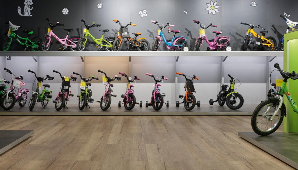 Szereg rowerków dziecięcych ustawionych w dwóch poziomach na ekspozycji sklepowej.