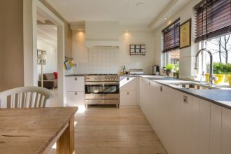 Jasna, biała kuchnia z meblami z płyty OSB, drewniana podłoga, drewniany stół na pierwszym planie