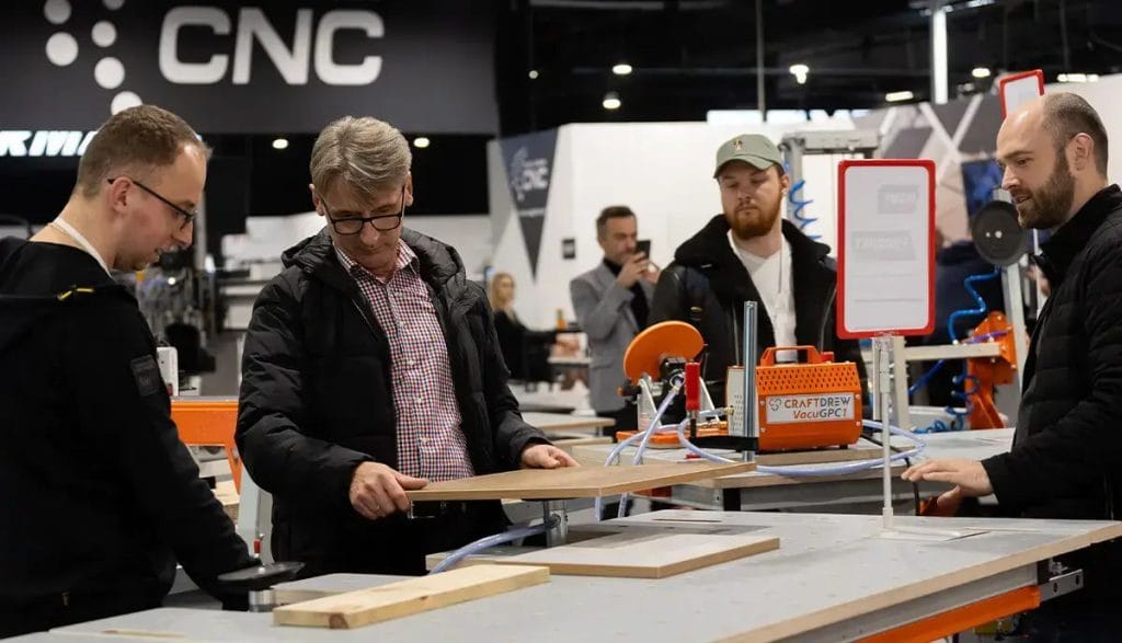 Mężczyzna oglądający drewnianą płytę na stanowisku z maszynami do obróbki drewna podczas targów branżowych.
