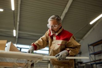 Widok z dołu na stolarza sprawdzającego wymiary podczas produkcji mebli w warsztacie. Fot. Drazen Zigic / Freepik.