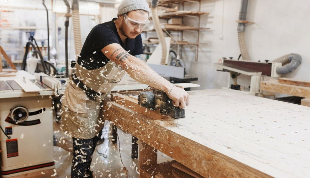Stolarz w goglach ochronnych przy produkcji mebli na wymiar.