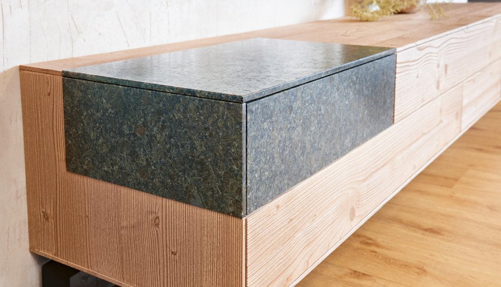 Lakiery wodne Bluefin z oferty Adler zaprezentowane na komodzie z dekorem drewnianym i kamiennym.