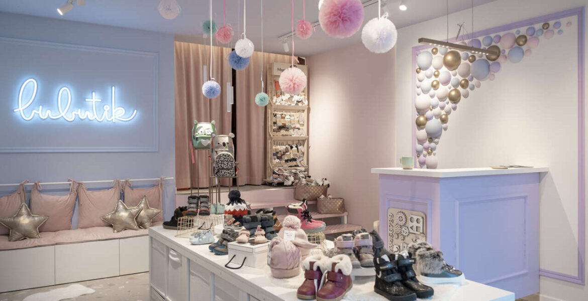 Aranżacja sklepu z obuwiem, projekt pracowni Fanajło Home Design Decor to ukłon w stronę dzieci. Na pierwszy plan wysuwają się kolorowe półkule na ścianie, które przywodzą na myśl bańki mydlane. Dopełnieniem kolorowej przestrzeni jest biel mebli potrzebnych do ekspozycji m.in. butów. Architektka Katarzyna Fanajło zadbała też o ukrycie pojemnego magazynu na buty za zasłoną. Kluczową rolę w sklepowej przestrzeni odgrywa jednak lada, która umożliwia wygodną obsługę. To miejsce, które powinno zostać dobrze doświetlone, dlatego w projekcie pojawiły się oprawy polskiej marki AQForm.
