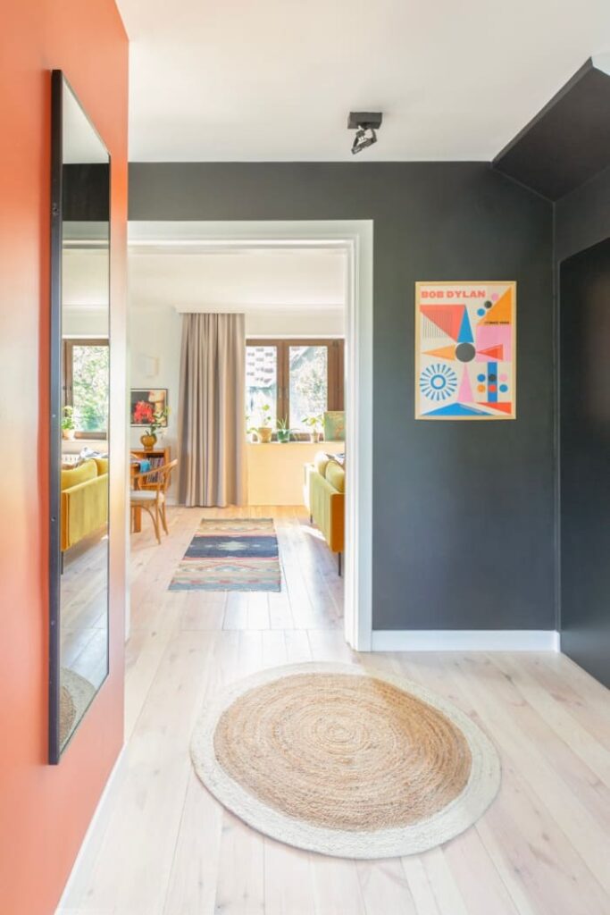 Zabawa kolorem, obecnym na ścianach w salonie, ma swoją kontynuację w holu przy schodach. Czerń i pomarańcz są̨ świetnym tłem dla wiszącego tu lustra.