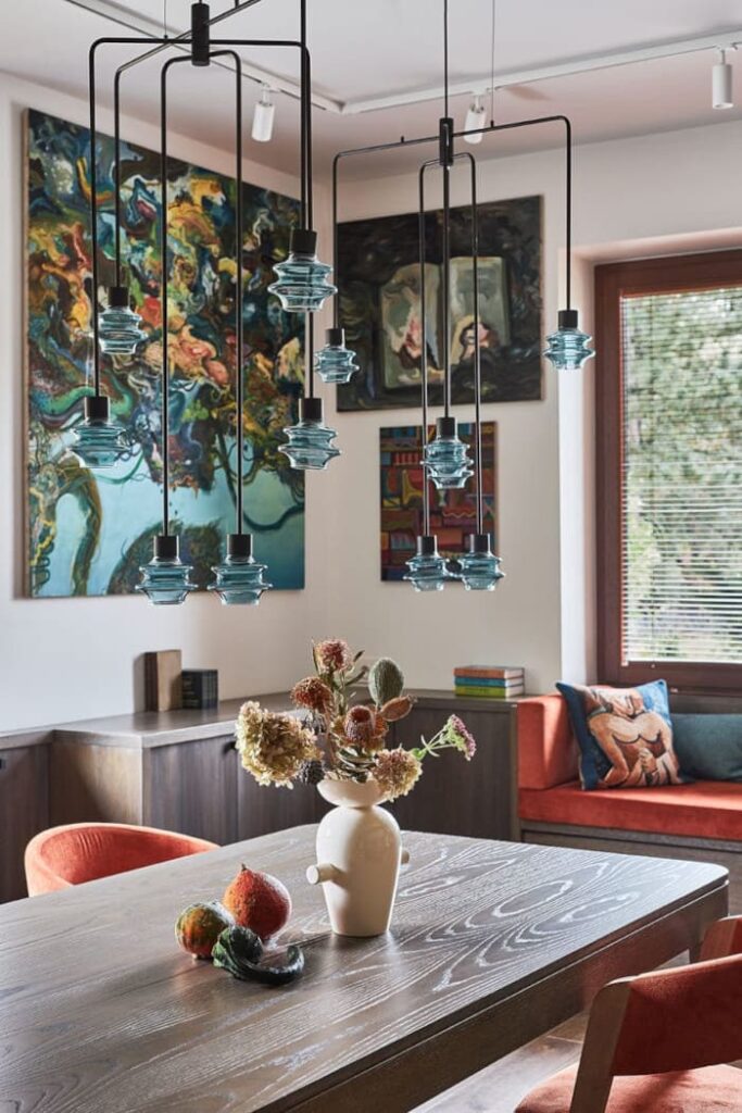 Za współczesnym żyrandolem w jadalni widzimy kolekcję obrazów Pawła Śliwińskiego. Dzieła sztuki doświetlono nastawnym światłem technicznym z szynoprzewodów sufitowych. Proj. arch. Roland Stańczyk.