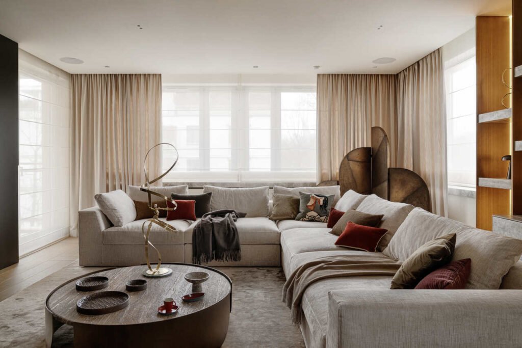 Wnętrze apartamentu na warszawskim Powiślu z wielką i wygodną sofą Meridiani, stolikiem z piaskowanego trawertynu szarego, a także robionym na zamówienie parawanem z blachy w trzech różnych kolorach. Po prawej widoczny jest wykonany na zamówienie regał z mosiądzu i szarego trawertynu.