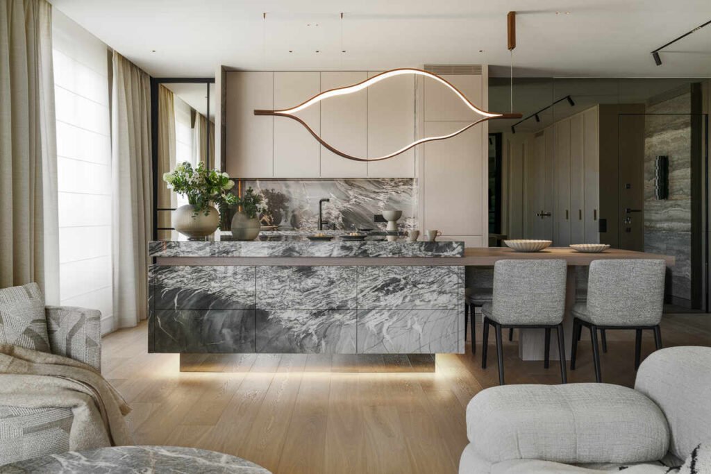 Kuchnia w apartamencie w Warszawie. Za lustrem ukryto drzwi wejściowe do mieszkania oraz wejście do pralni i łazienki. Wyspa wykonana z kwarcytu odpornego na wszelkie zabrudzenia, nad wyspą wisząca lampa Henge. Krzesła Minotti, fotele po lewej stronie Minotti, sofa B&B Italia. Cokół wyspy z poświatą LED, aby wyspa sprawiała wrażenie lewitującej.