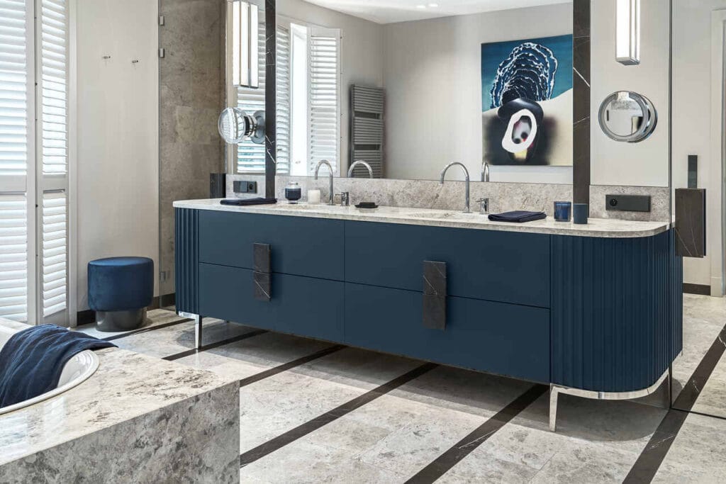 Łazienka w domu na Saskiej Kępie, z pięknym meblem robionym na zamówienie. Kamienne uchwyty w meblu i na drzwiach do prysznica oraz drzwiach lustrzanych kierowanych do toalety. Wanna Bette metalowa z lekkim kołnierzem wywiniętym na kamień. Pasy na podłodze nawiązują do modernizmu, gdyż w tym stylu jest zbudowana architektura tego domu.