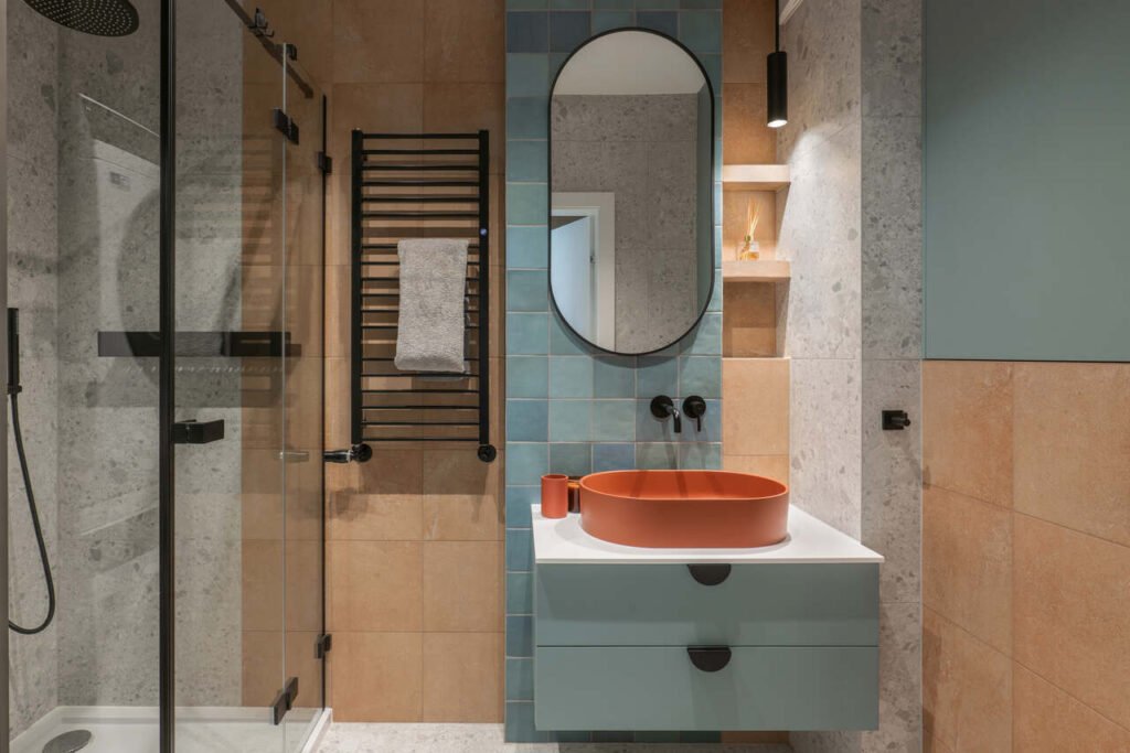 W łazience są trzy rodzaje płytek ściennych – w kolorze ceglastym, aquamarine i szarości, proj. KODO.