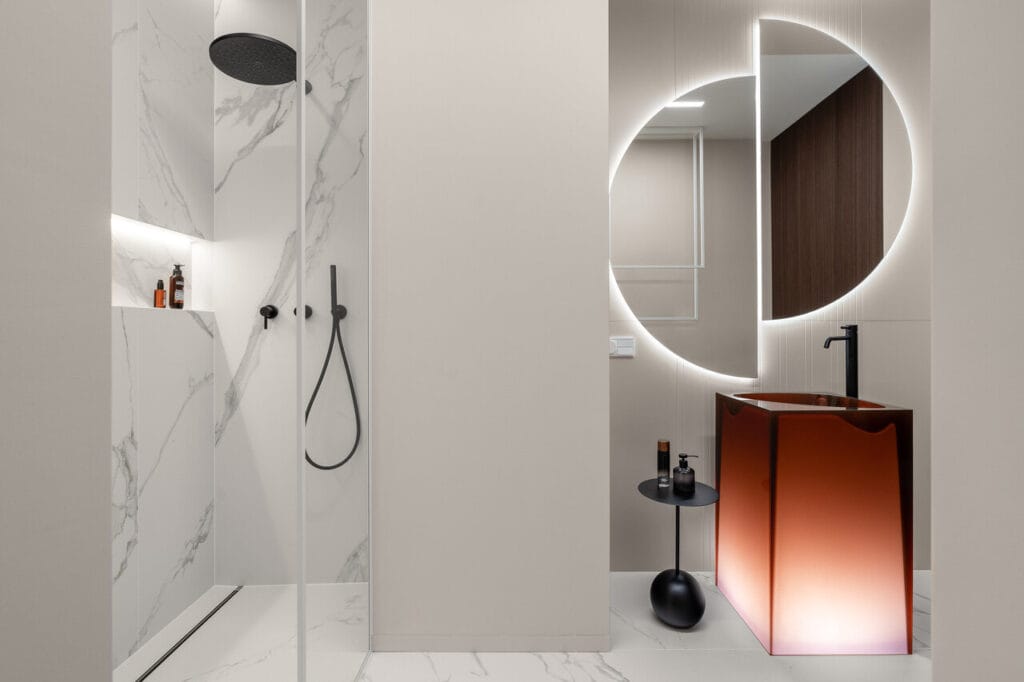 Łazienka gościnna w apartamencie wakacyjnym w inwestycji Brabank w Gdańsku. Połączenie klasycznego wzoru marmuru callacata z delikatnym odcieniem beige na ścianach. Całość to doskonałe i ponadczasowe tło dla pięknej podświetlanej umywalki i luster marki Antonio Lupi. Fot. Katarzyna Seliga-Wróblewska, Marcin Wróblewski / Fotomohito.