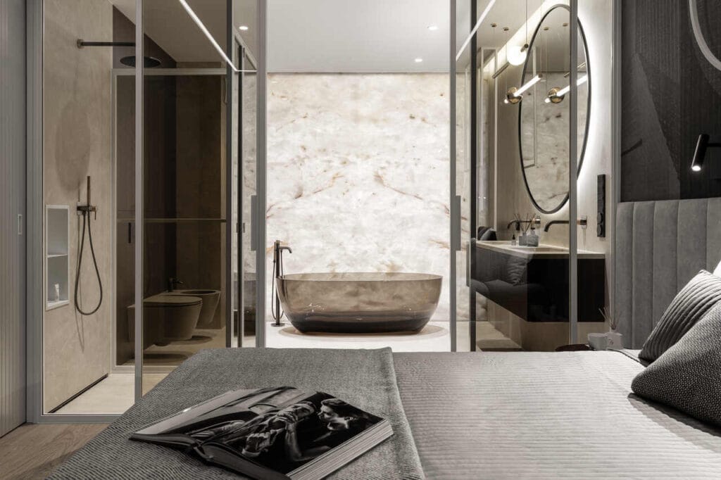 Łazienka w sypialni w apartamencie wakacyjnym w inwestycji Brabank w Gdańsku. Kwintesencja połączenia natury i doskonałego designu. Główna ściana, przy której stoi wanna marki Antonio Lupi, wykonana z podświetlanego, naturalnego Onyxu. Całość wnętrza utrzymana w ciepłej tonacji ze spieku kwarcowego Laminam Cava Diamond Cream i elementami stalowymi wykonanymi na zamówienie. Fot. Katarzyna Seliga-Wróblewska, Marcin Wróblewski / Fotomohito.