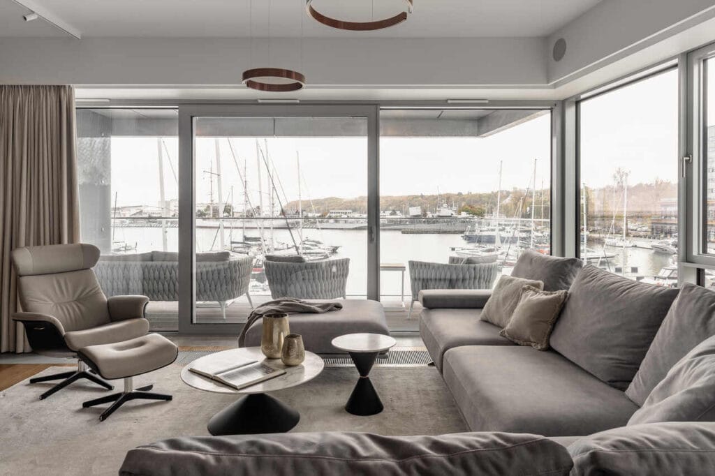 Strefa wypoczynkowa dwupoziomowego apartamentu wakacyjnego w inwestycji Yacht Park Gdynia. Realizacja wykonana przy współpracy z biurem projektowym Mitotu. Dzięki dużym przeszklonym witrynom mamy zachowany piękny widok na gdyńską marinę, która wita nas już od wejścia do apartamentu. Całość dopełniają wyjątkowe lampy wiszące od Occhio, sofa Olta, fotel Conform i stoliki Midj. Fot. Katarzyna Seliga-Wróblewska, Marcin Wróblewski / Fotomohito.