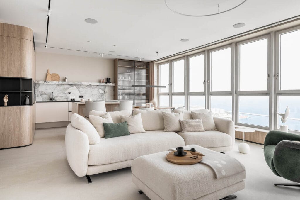 Strefa wypoczynkowa z aneksem kuchennym i jadalnią w apartamencie na 26 piętrze inwestycji Sea Towers w Gdyni. Widok z okien to ozdoba tego wnętrza i magnes, który nie pozwala oderwać oczu od błękitu nieba i Zatoki Gdańskiej. Stonowane, ponadczasowe wnętrza, z delikatnymi detalami i ozdobami zdecydowanie podkreślają rangę samej lokalizacji. Spiek Patagonia, a także piękna forma sofy Olta są tu zdecydowanymi faworytami. Fot. Katarzyna Seliga-Wróblewska, Marcin Wróblewski / Fotomohito.