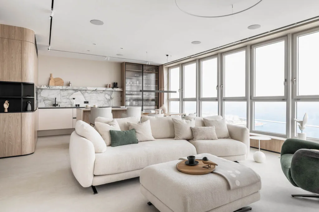 Strefa wypoczynkowa z aneksem kuchennym i jadalnią w apartamencie na 26 piętrze inwestycji Sea Towers w Gdyni. Widok z okien to ozdoba tego wnętrza i magnes, który nie pozwala oderwać oczu od błękitu nieba i Zatoki Gdańskiej. Stonowane, ponadczasowe wnętrza, z delikatnymi detalami i ozdobami zdecydowanie podkreślają rangę samej lokalizacji. Spiek Patagonia, a także piękna forma sofy Olta są tu zdecydowanymi faworytami. Fot. Katarzyna Seliga-Wróblewska, Marcin Wróblewski / Fotomohito.