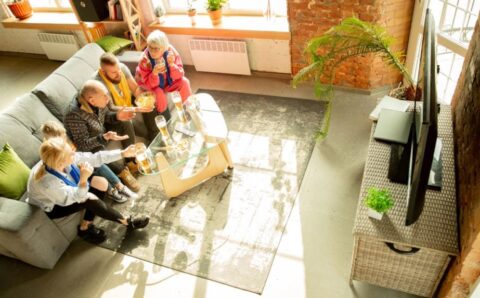 Rodzina przy posiłku na szarej kanapie przed telewizorem